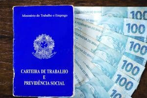 Carteira de trabalho e notas de 100 reais representando como sacar o pis/pasep