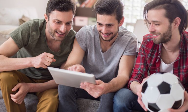 amigos olhando para o tablet e segurando bola de futebol, apostas