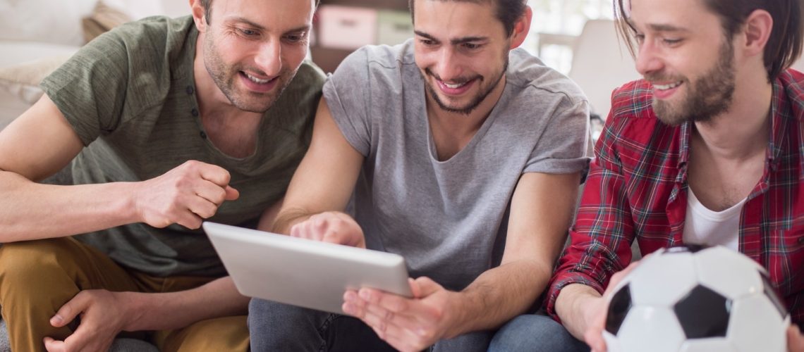 amigos olhando para o tablet e segurando bola de futebol, apostas