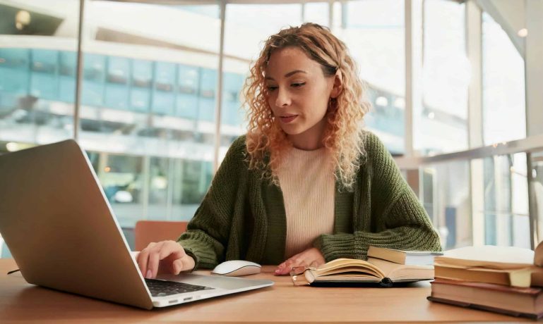 Imagem de uma mulher em frente ao seu notebook representando uma pessoa que estudo e trabalho