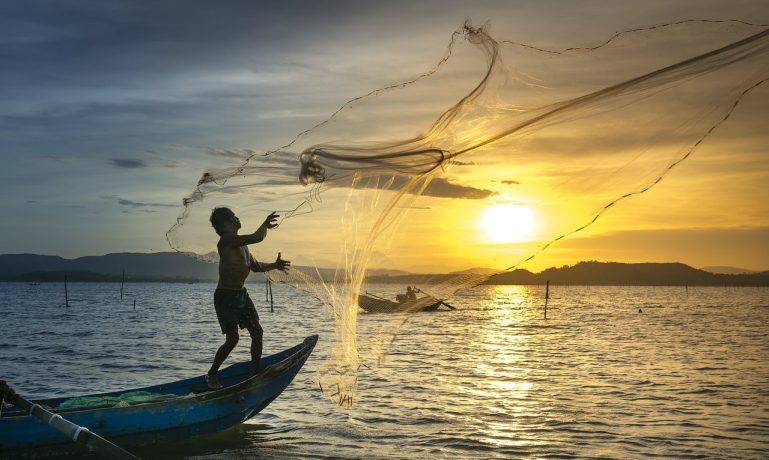 Pescador jogando sua rede no mar e possui Seguro defeso