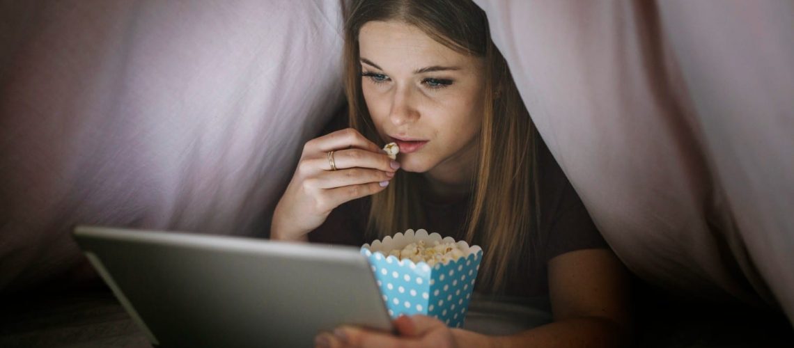 mulher debaixo do coberto assistindo filme no tablet