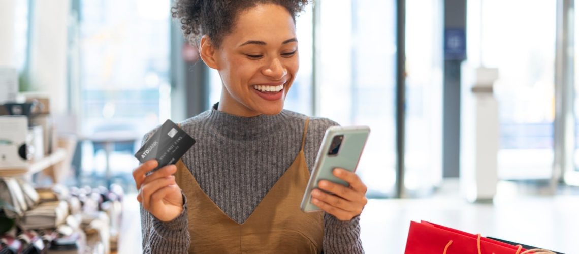 mulher sorrindo pagando compra pelo celular com cartão de crédito