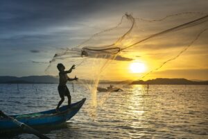 Pescador jogando sua rede no mar e possui Seguro defeso