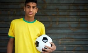 jovem com camiseta do Brasil segurando bola de futebol