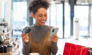 mulher sorrindo pagando compra pelo celular com cartão de crédito